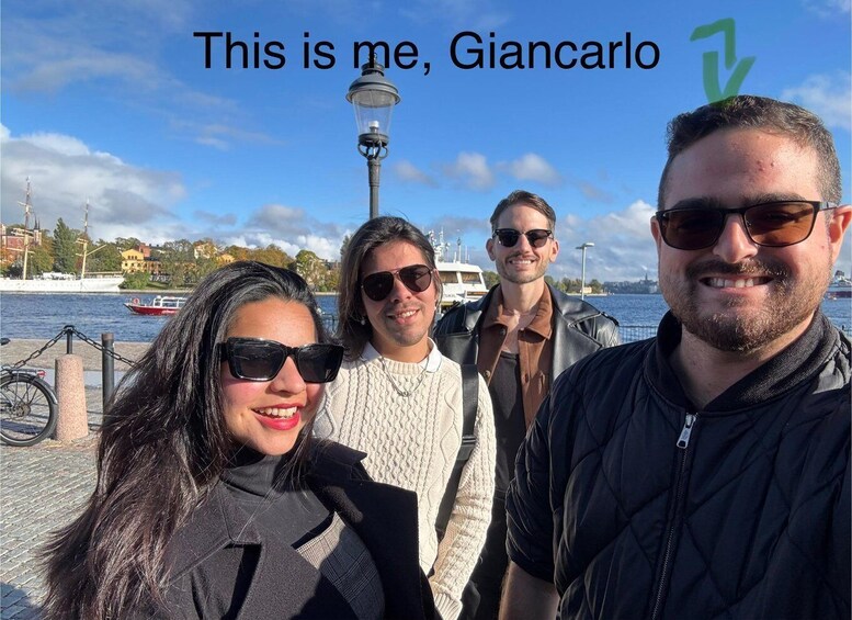 Four people standing by a waterfront with a boat in the background. 4