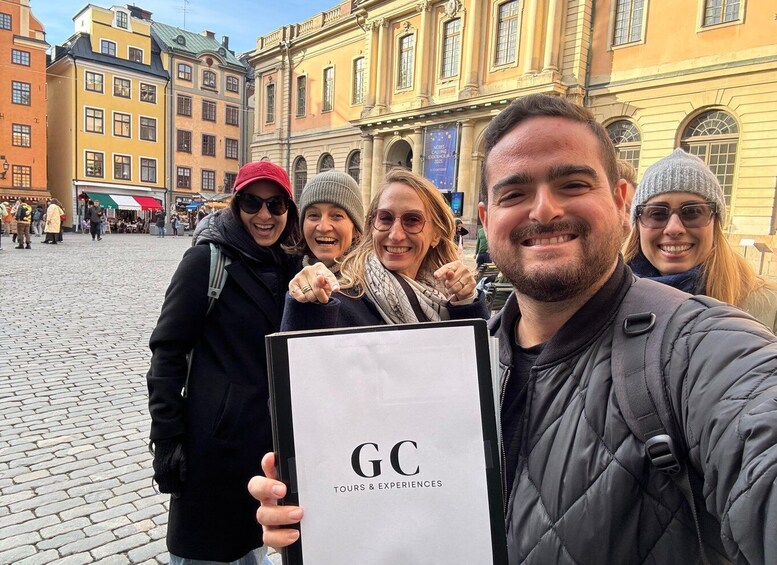 A group of people in a cobblestone square with historic buildings in the background. 1