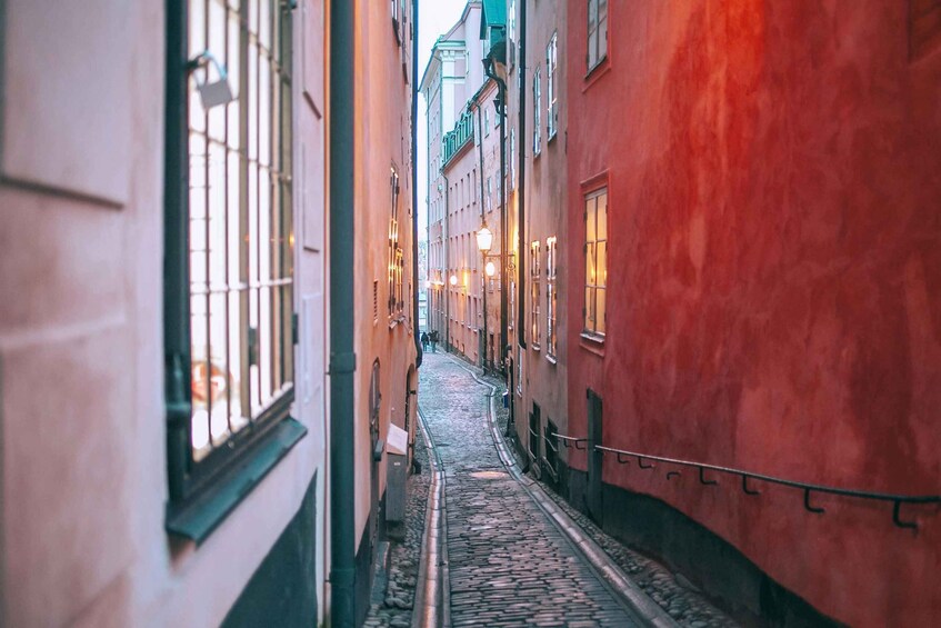 A narrow cobblestone street flanked by buildings with barred windows and warm lighting. 3