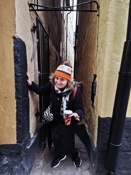 A person standing in a narrow alleyway with a black and yellow wall, holding a cup. 2