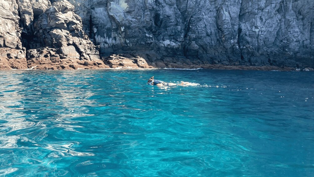 A swimmer in clear blue water with rocky cliffs in the background. 3