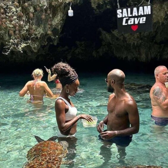 A group of people in a natural water setting with a cave entrance labeled 'SALAAM Cave'. 2