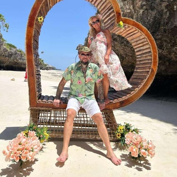A man and a woman sitting in a circular wicker structure on a sandy beach with flowers. 4