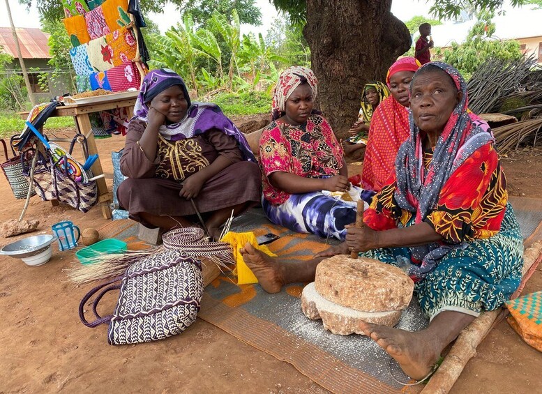 Women engaged in weaving, seated on the ground with colorful fabrics and tools. 1