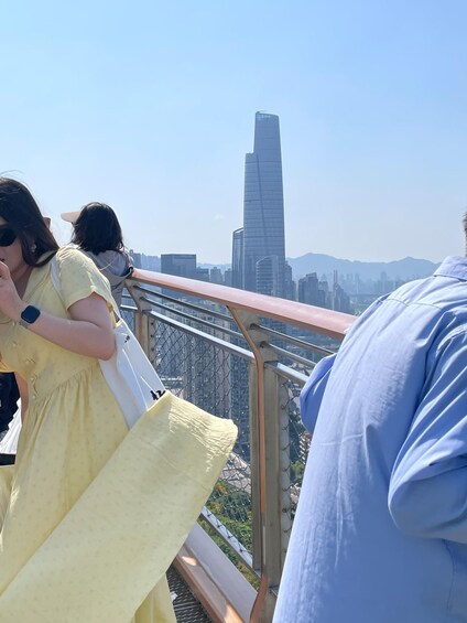 A person in a yellow dress standing on a bridge with a cityscape and a tall skyscraper in the background. 5