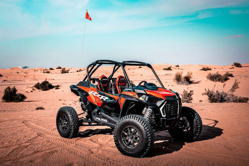 A Polaris RZR off-road vehicle in a desert with sand dunes and sparse vegetation. 1