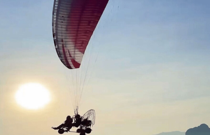 A paraglider with a red and white parachute descending towards the sun. 5