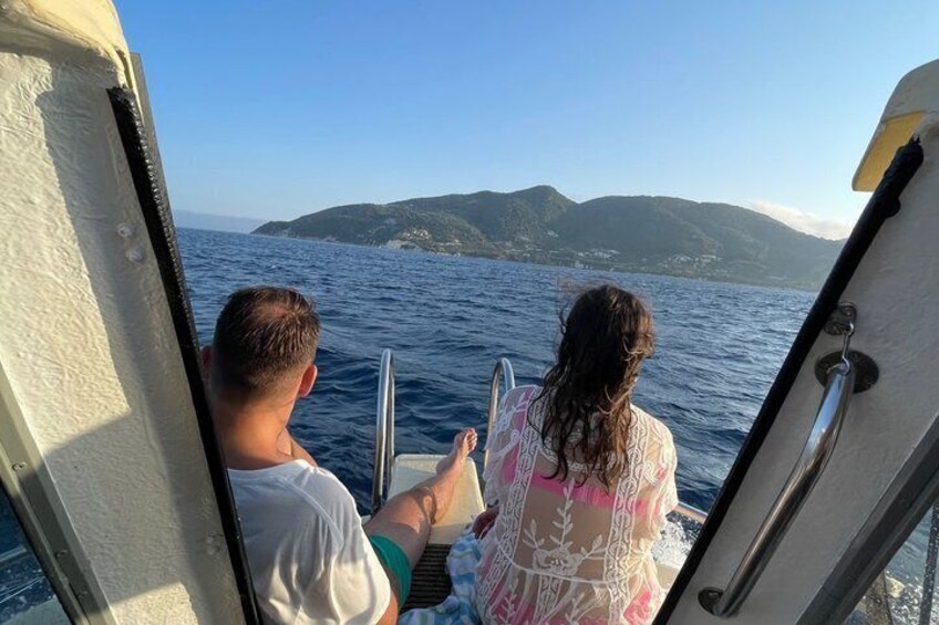 Two people on a boat with a mountainous coastline in the background. 5