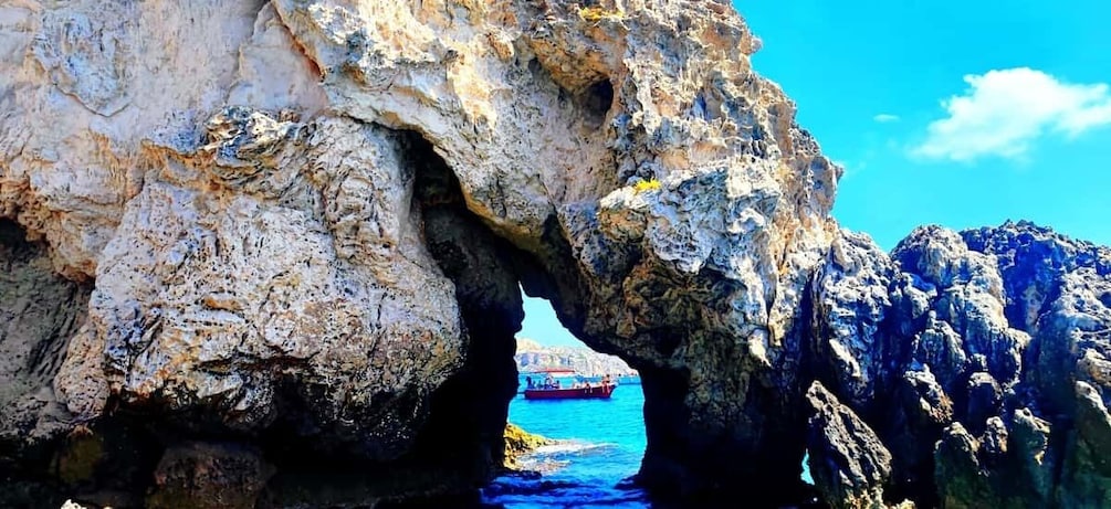 A rocky coastline with a natural arch formation and a boat in the water. 2