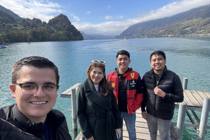 A group of people on a wooden dock by a lake with mountains in the background. 5