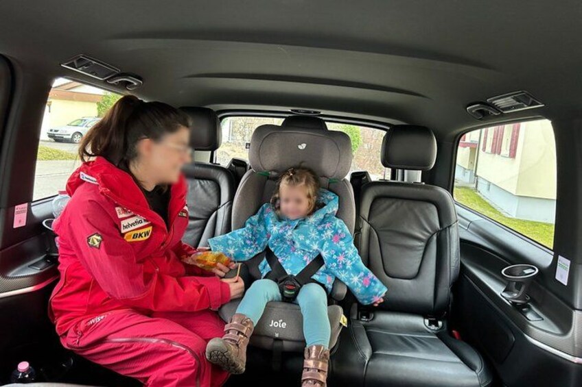 A woman in a red racing suit and a child in a blue snowflake-patterned coat seated in a car's back seat. 3