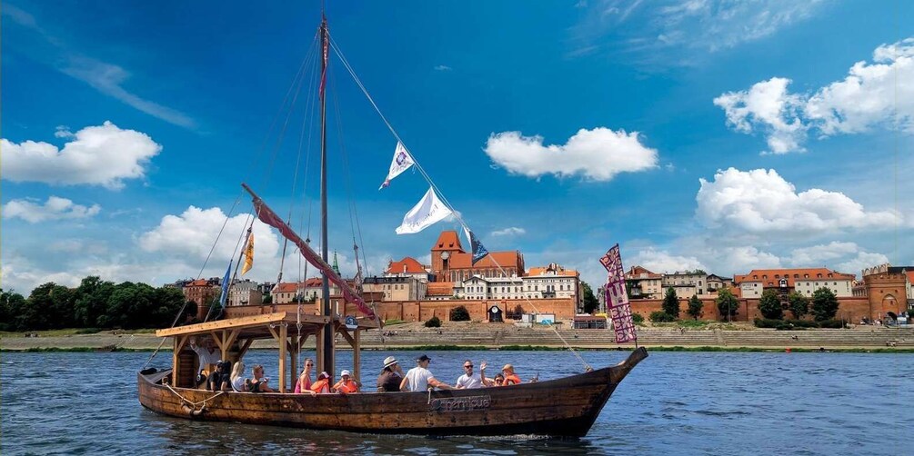 A wooden boat with passengers on a river, a castle in the background, and a clear blue sky. 2