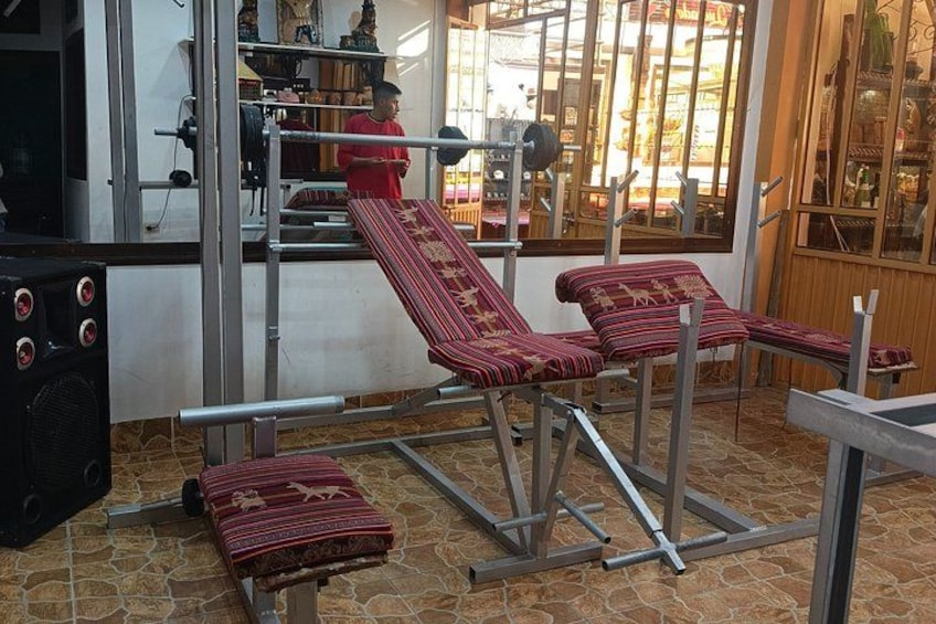 A massage table with a red patterned cover, a massage chair, and a massage table in a room with a tiled floor and a window with a view of the street outside. 2