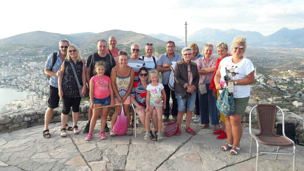 A group of people standing on a stone platform with a city and mountains in the background. 3