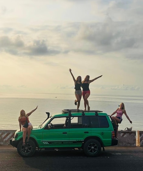 A green SUV parked by the water with four people standing on it. 2