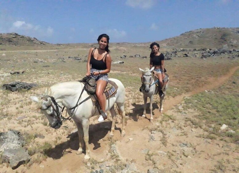 Two women riding donkeys on a dirt path in a barren landscape. 5