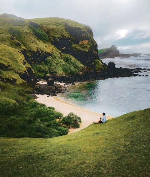 A coastal landscape with a grassy hill, a sandy beach, and a rocky shoreline. 5