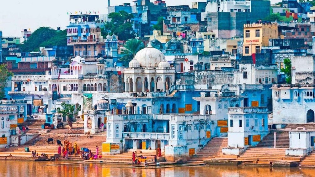 A densely packed urban area with historic buildings, a prominent white-domed structure, and a river with people and boats. 1