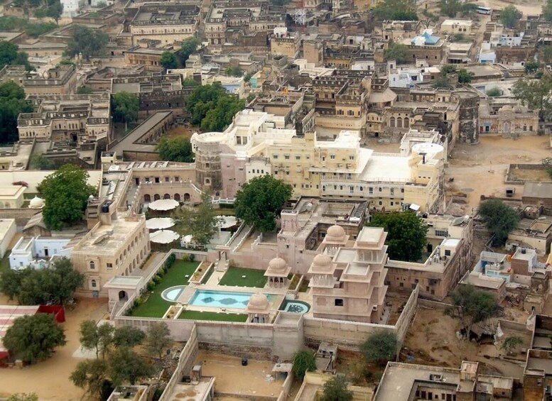 An aerial view of a historic city with dense architecture, a prominent building with domes, and a central courtyard with a pool. 2