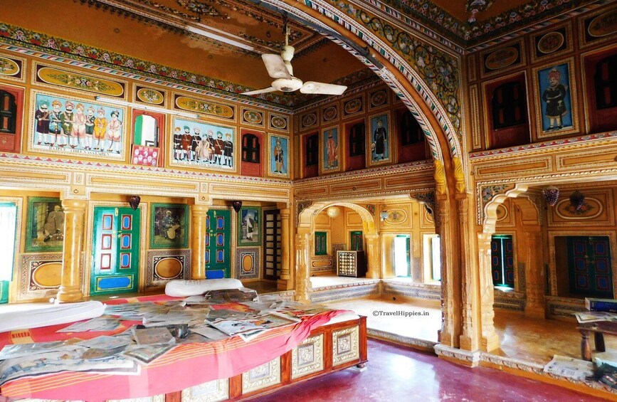 A richly decorated interior with intricate murals, a ceiling fan, and a large bed with a red bedspread. 4