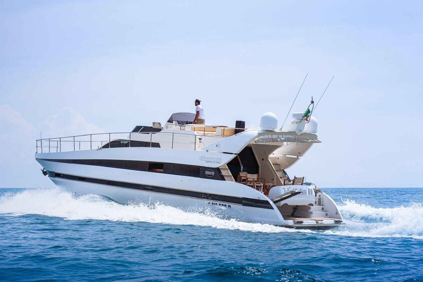 A white yacht with a person standing on the deck, moving through the water. 1