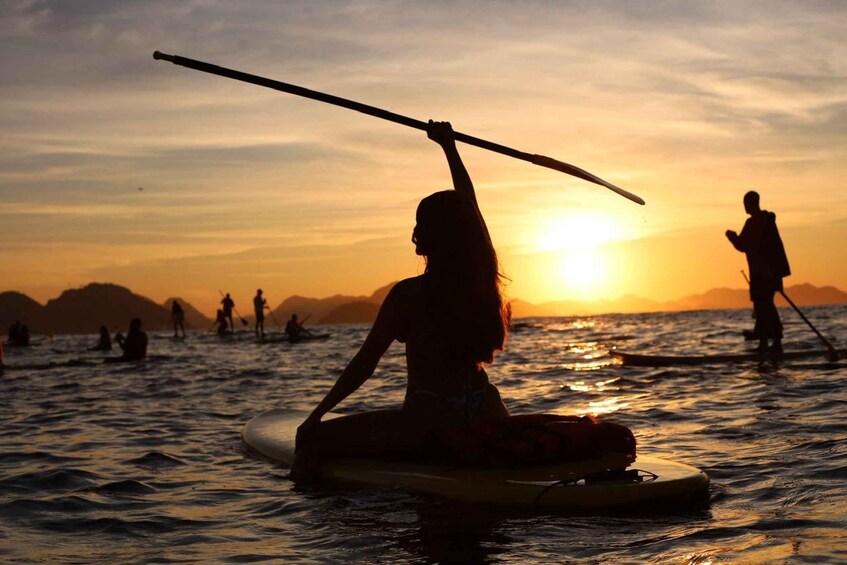 A person sitting on a paddleboard in the ocean at sunset. 3