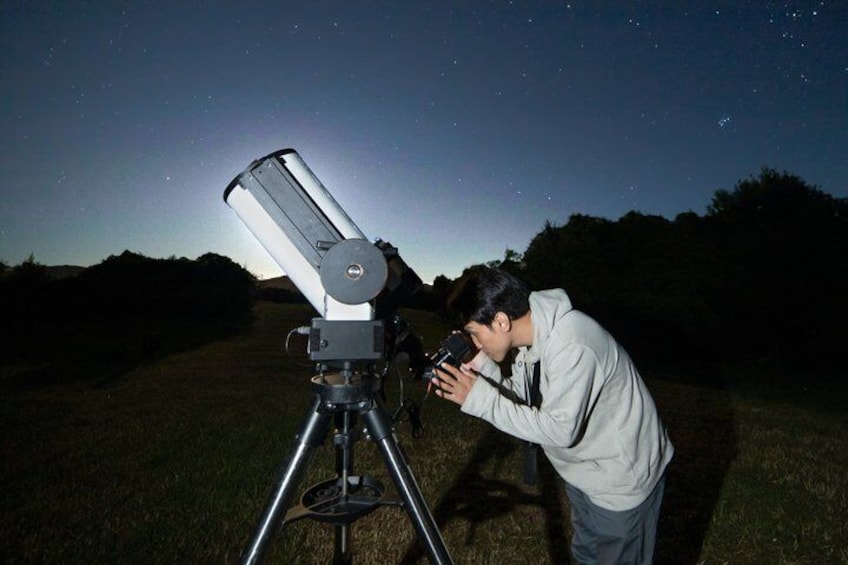 A person using a telescope in a grassy field at night. 4
