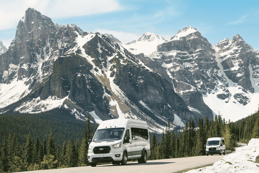A white RV driving on a snow-covered mountain road with rugged peaks in the background. 2
