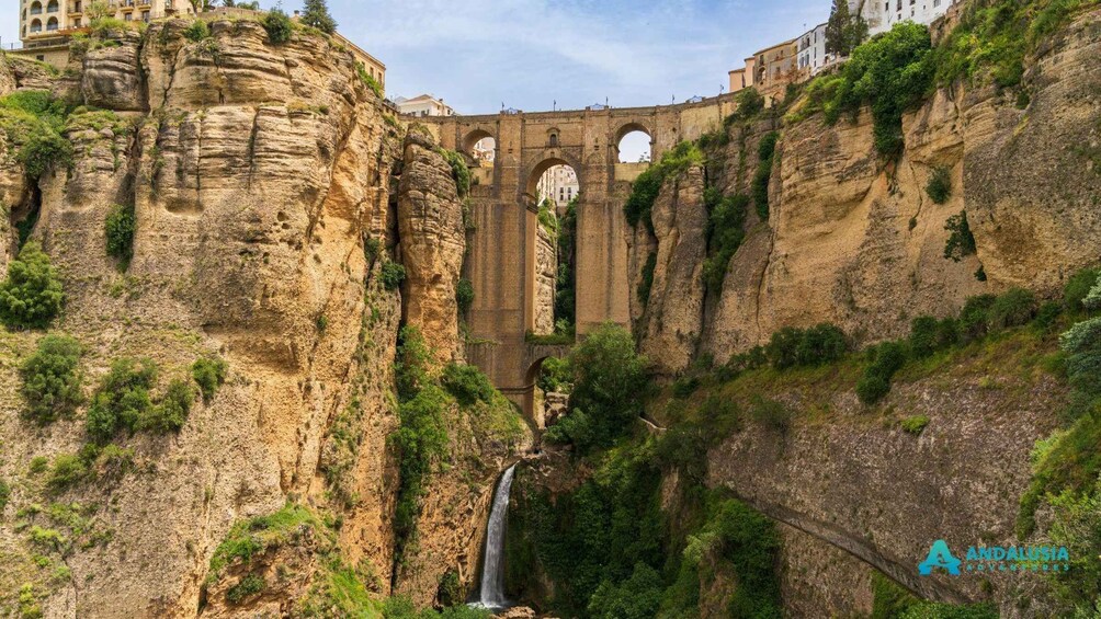 A historic stone bridge with arches, a waterfall, and lush greenery. 1