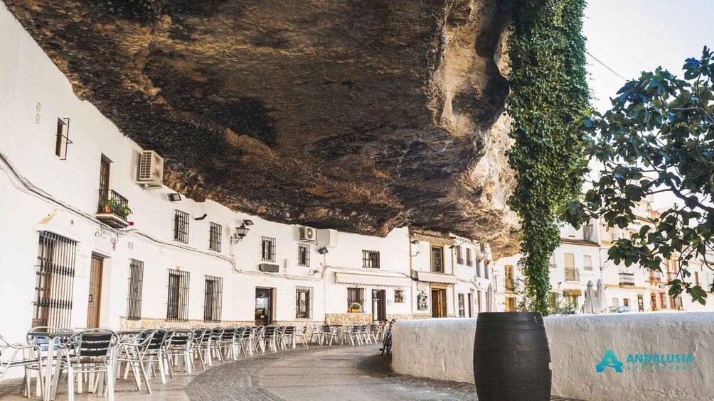 A street with white buildings, a large rock formation, and metal chairs. 2