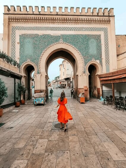 A woman in a red dress walking through a historic archway with intricate tile work. 3