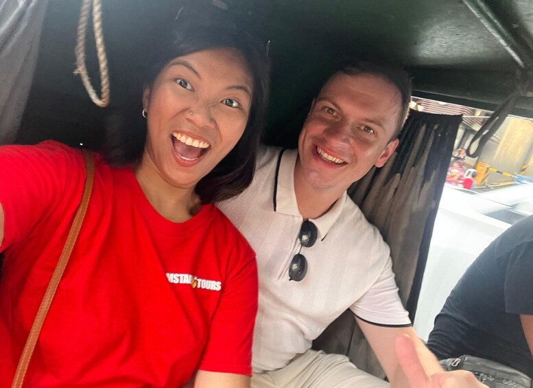 Two people in a vehicle, one wearing a red shirt with a logo and the other in a light-colored shirt with sunglasses. 3