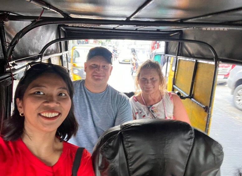 Three people inside a vehicle with a yellow exterior, likely a tuk-tuk, with a black bag on the seat. 4