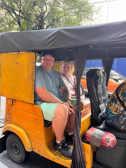 Two people sitting in a yellow auto-rickshaw with a black canopy. 5