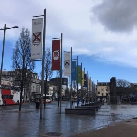 A wet urban square with flags, a bus, and buildings in the background. 1