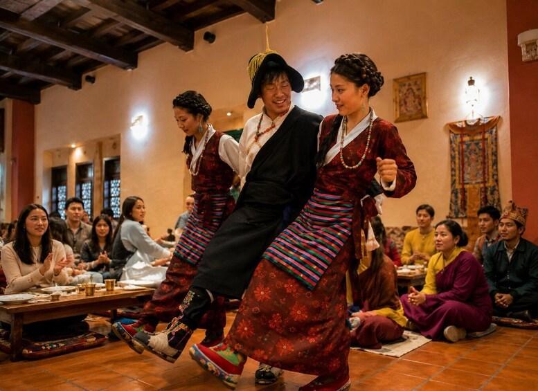 A group of people in traditional attire, some seated and some standing, in an indoor setting with wooden beams and patterned textiles. 2