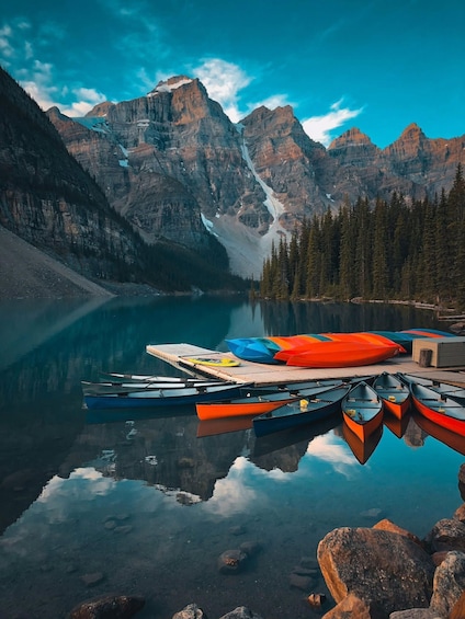 A calm lake with boats, a dock, and a mountain range in the background. 2