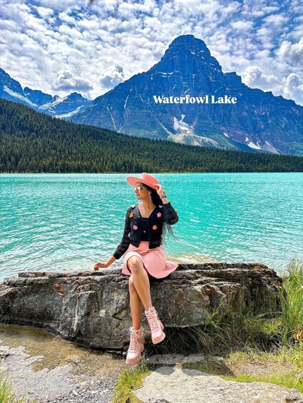 A person sitting on a rock by Waterfowl Lake with mountains in the background. 3