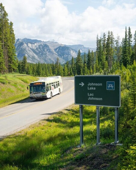 A bus on a road with a sign indicating directions to Johnson Lake and Lac Johnson. 4