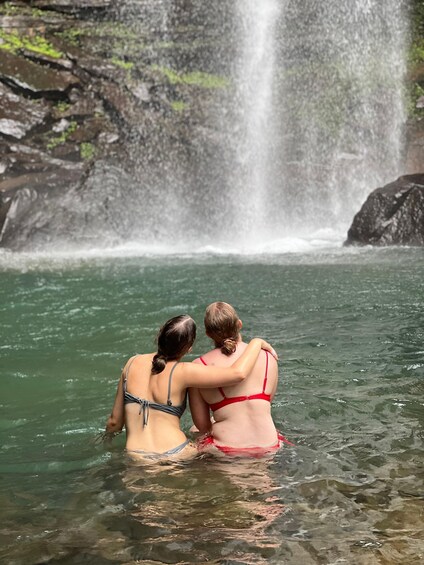 Two people in a clear pool with a waterfall in the background. 2