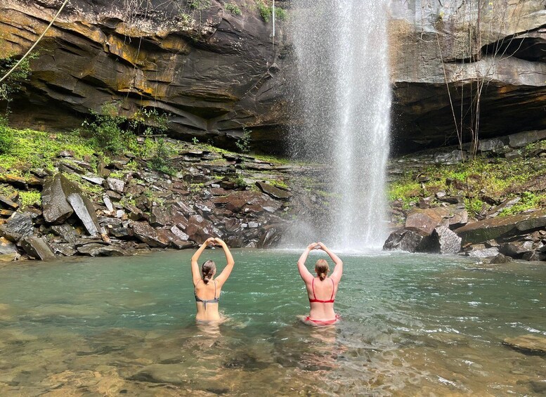 Two people making heart shapes in the water with a waterfall in the background. 3