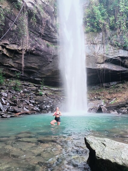A woman kneeling in a clear pool of water with a waterfall in the background. 1