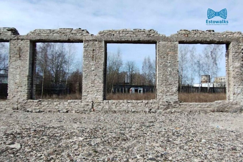 A row of stone ruins with windows, surrounded by a gravel area and trees in the background. 4