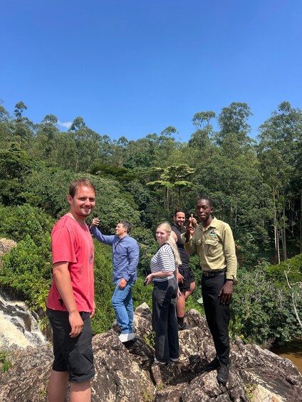 A group of people standing on rocks by a river in a forested area. 2