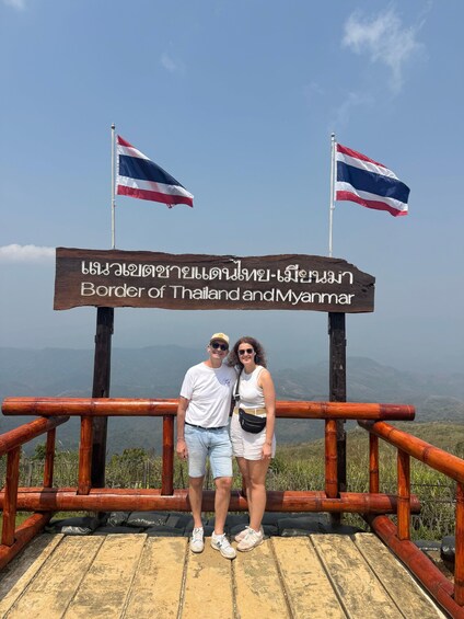 A wooden sign with flags and text indicating the border of Thailand and Myanmar. 3