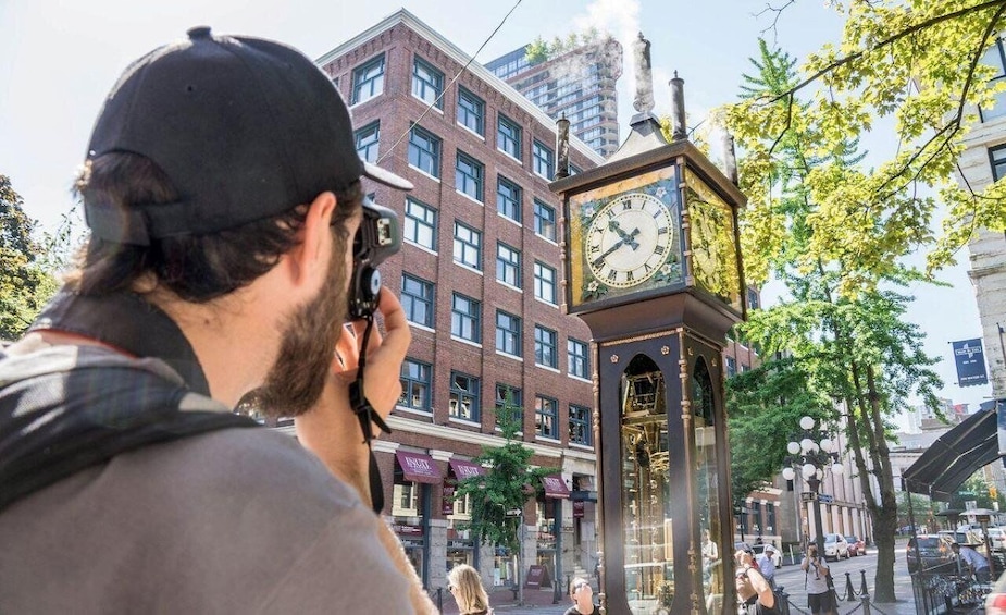 A person taking a photo of a clock tower in an urban setting. 1