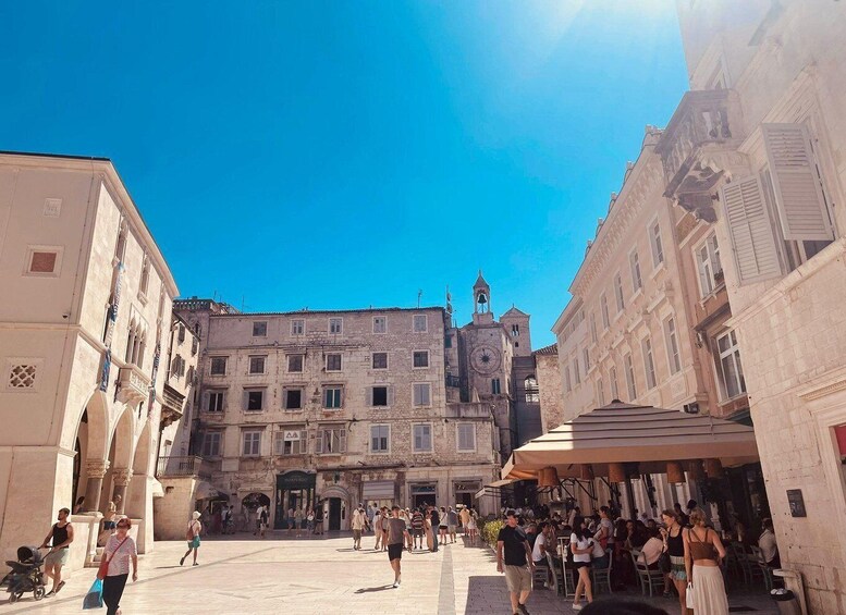 A bustling square with historic buildings, a prominent clock tower, and outdoor seating areas. 4