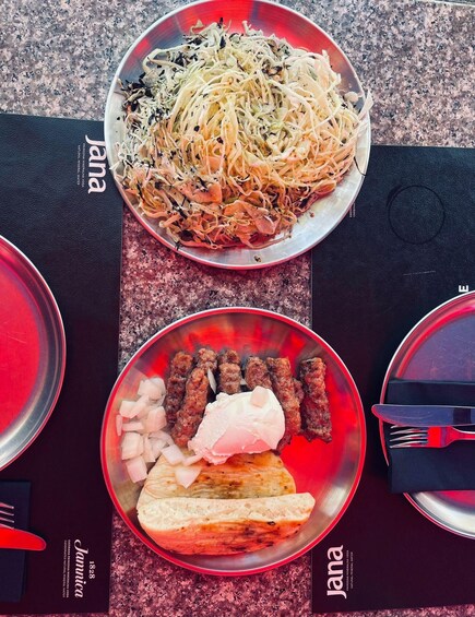 A table with two plates of food, one with noodles and vegetables and the other with meat and bread. 3