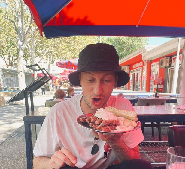 A person sitting at an outdoor table under a red umbrella, holding a plate with food. 5