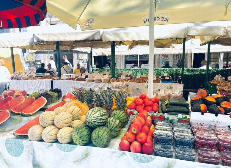 A fruit and vegetable market with various stalls selling produce like watermelon, apples, and berries. 2